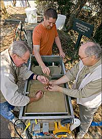 Colonial Williamsburg archaeologist Steve Archer, center, with volunteers Tony Herrmann, left, and Jim Bowers, sift artifacts from a soil sample in a flotation machine to recover bits and pieces of plant material and other information earlier methods missed.
