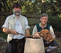 Holding bog iron ore, Colonial Williamsburg master blacksmith Ken Schwarz with journeyman Shelton Browder at a model of a bloomery.