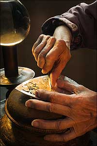 Strong and supple, practiced and sure, the hands of silversmith Gayle Clarke pierce a piece of plate by the magnified light of a water-filled globe lamp.