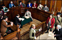 A felony trial in British Virginia took place in the General Court of Williamsburg’s Capitol, the governor usually presiding, with the Governor’s Council sitting in judgment. In front of the railing, left to right, witness Ken Treese, defendant Bill Rose, bailiff Steve Holloway, and prosecutor Jack Flintom. At the green desk, Ben Knecht, left, and Mark Couvillon. Seated clockwise In the back, from lower left, Russ Wells, Alex Clark, Phil Shultz, Frank Megargee, Chris Allen, governor Scott Green, Robin Reed, Mike Pfeiffer, Joe Musika, John Needre, and Ken Zeller.
