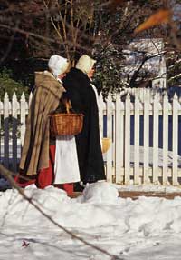 Cloaked against a sunny chill, two costumed interpreters follow a path through the remains of a Williamsburg snowfall. 
