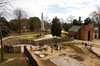 Inside the fort at Jamestown, in the cellar seen just below the back wall of a stone foundation, archaeologists found a pendant that dates to the Virginia colony’s earliest years. A seventeenth-century church tower and the 1907 tercentenary obelisk are also seen.