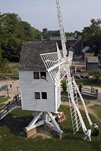 Mill hands, in the persons of Colonial Williamsburg interpreters and tradespeople, unfurl the sails over the vanes of the towering wind-powered machine at the rear of the Peyton Randolph House. 