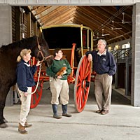 Coach and Livestock’s Karen Smith, Elaine Shirley, and Richard Nicoll, holding hoof, feather, and wheel, in the Colonial Williamsburg stables.