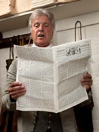 Dennis Watson, as Alexander Purdie, reads from The Virginia Gazette.
